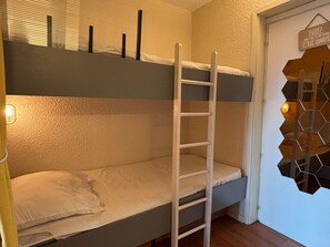 Una cama litera con escalera, una puerta con un letrero y un espejo hexagonal en la pared.