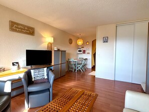 Ein Wohnzimmer mit Fernseher, einer Couch, einem Couchtisch und einem Essbereich mit Stühlen und einem Tisch.