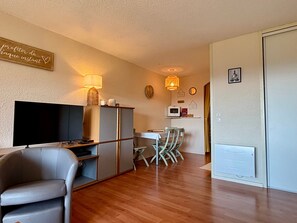 Una sala de estar con televisor de pantalla plana, un sofá, una mesa de comedor con sillas y una zona de cocina con microondas.