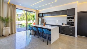 A modern kitchen with a large island, bar stools, dark cabinets, and built-in appliances. - Beautiful villa with swimming pool at Argan Golf Resort (Marrakesh)