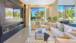 A modern living room with a large TV, a sofa, a coffee table, and a view of a garden. - Beautiful villa with swimming pool at Argan Golf Resort (Marrakesh)