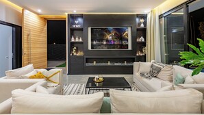 A modern living room with a large flat-screen TV, comfortable seating, and a decorative shelf with items. - Beautiful villa with swimming pool at Argan Golf Resort (Marrakesh)