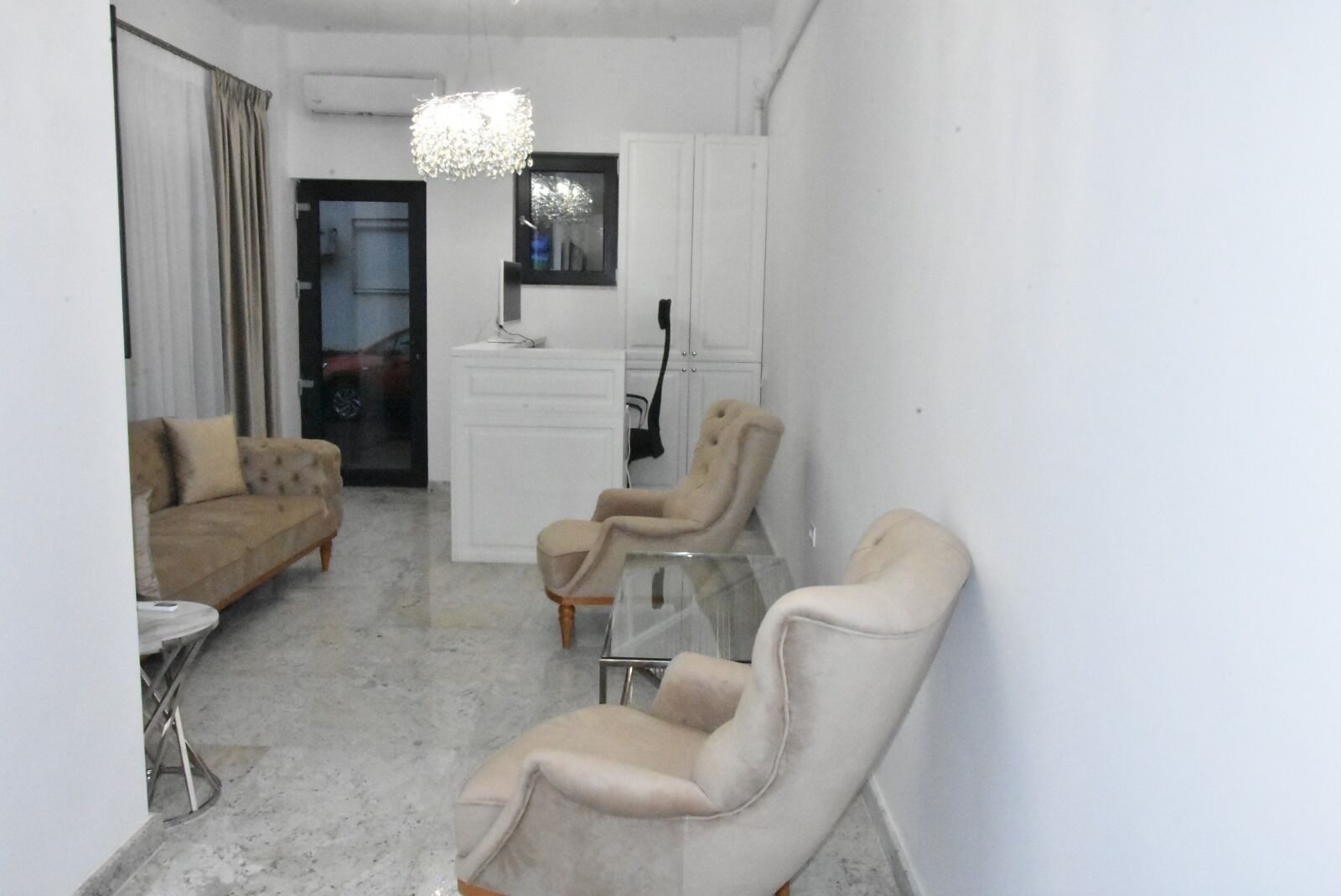 A living room with a sofa, two armchairs, a glass coffee table, and a chandelier.