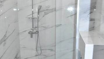 Un baño moderno con ducha envuelta en vidrio, inodoro blanco y paredes de mármol.