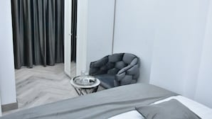 Et lille, moderne soveværelse med en seng, en grå lænestol, et rundt bord med et bakke og et stort spejl.