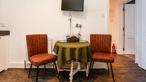 Una habitación con una mesa, dos sillas, un televisor montado en la pared y un extintor.