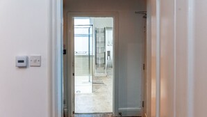 Pasillo que conduce a un baño con puerta de vidrio, un perchero y una zona de ducha visible.