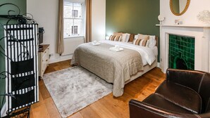 Un dormitorio con cama, chimenea, espejo y una silla.
