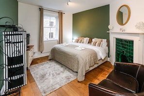 A bedroom with a bed, a fireplace, a mirror, and a chair.