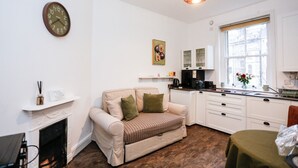 Una sala de estar acogedora con chimenea, un sofá, una mesa de comedor y una zona de cocina con armarios y una ventana.