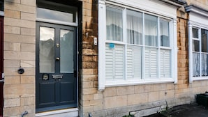 Une maison de ville avec une porte d’entrée sombre, une fenêtre ornée de volets blancs et une façade en briques.