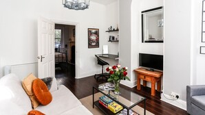 Un salon moderne avec un canapé blanc, une table basse avec des magazines, un téléviseur et une cheminée.