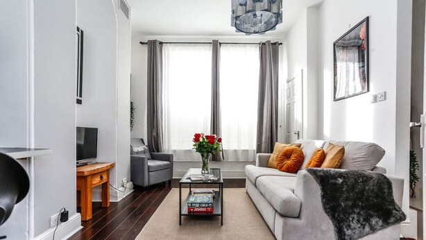 Un salon moderne avec un canapé gris, une table basse sur laquelle sont posés des livres, un téléviseur et une grande fenêtre ornée de rideaux gris.