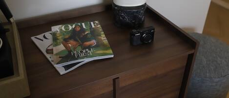 A wooden nightstand with a camera and magazines.