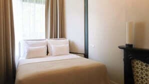 A hotel room with a bed, curtains, a wall-mounted light, and a chair. - Dam Residence's Heritage Rooms (Zaandam)