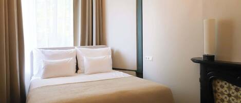 A hotel room with a bed, curtains, a wall-mounted light, and a chair.