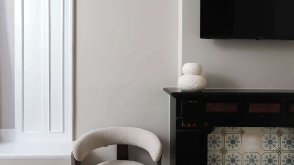 Une pièce avec une chaise blanche, une cheminée ornée de carreaux décoratifs et un téléviseur fixé au mur.