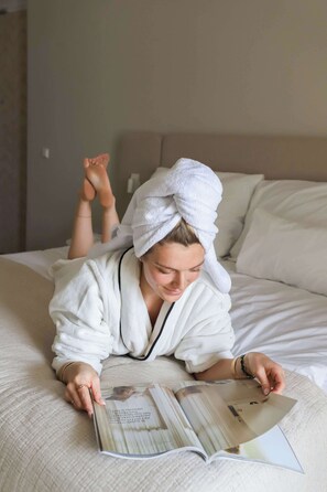 Une personne allongée sur un lit, une serviette blanche sur la tête, est en train de lire un magazine.