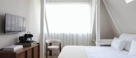 A hotel room with a bed, a TV, a desk with a coffee maker, a chair, and a window with curtains.