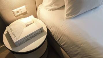Een netjes opgemaakt bed met witte lakens en kussens, een nachtkastje met een lamp, en twee boeken met de titels 'The Kinfolk Home' en 'Live Beautiful'.