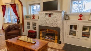 A cozy living room with a fireplace, a leather armchair, a wooden coffee table with candles, and a bookshelf. - The Speakeasy-Hot Tub-Pet Friendly-Downtown-AC (Red Lodge)
