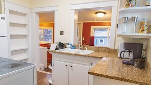 A kitchen with white cabinets, a granite countertop, a coffee maker, and a window with a view of a house. - The Speakeasy-Hot Tub-Pet Friendly-Downtown-AC (Red Lodge)