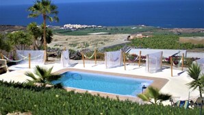 A pool area with a view of the sea, palm trees, and a distant town.