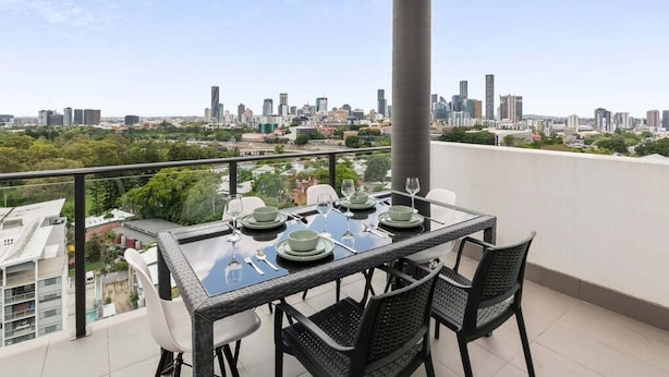 Un balcon avec une table dressée pour quatre personnes, offrant une vue sur le paysage urbain.