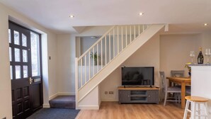 Un salon moderne avec un escalier, un téléviseur à écran plat, un coin repas avec une table et des chaises, et un bar avec un tabouret.