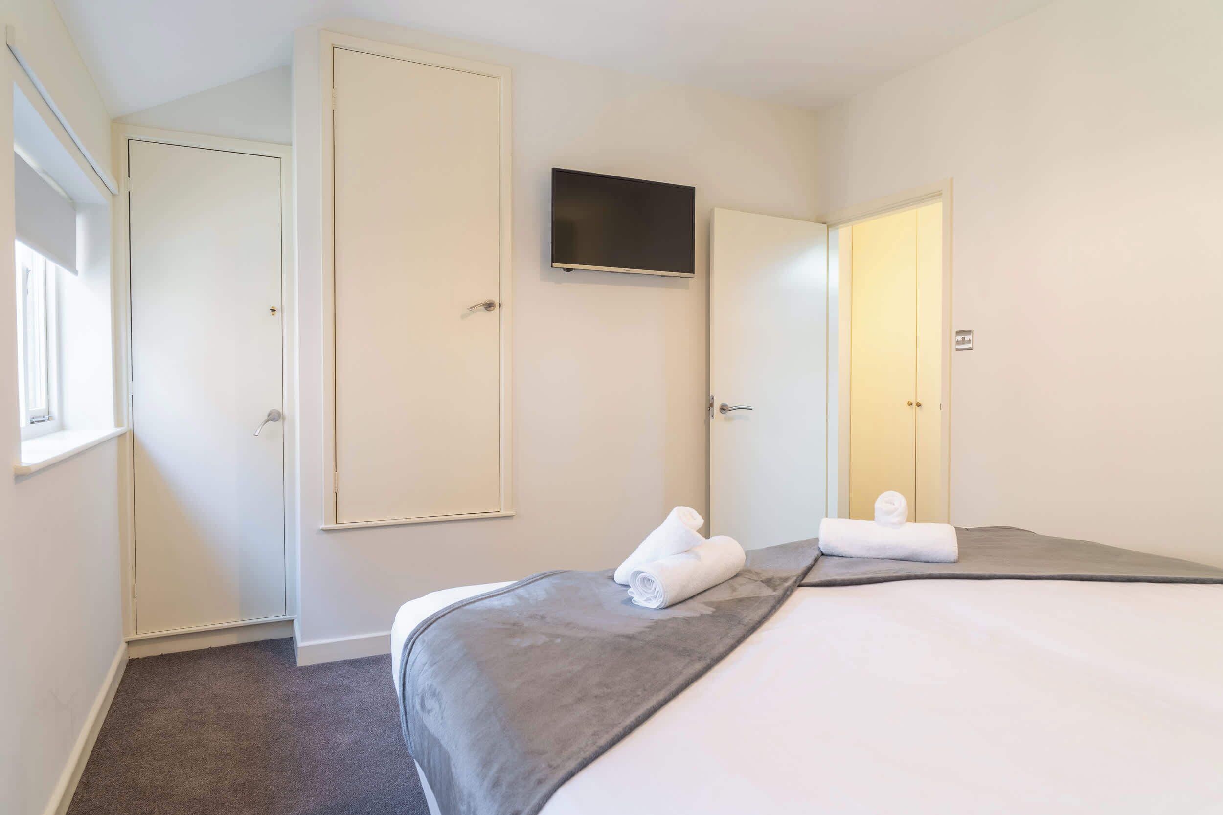 Una camera d'albergo con un letto, una TV fissata al muro e una porta che dà su un'altra stanza.