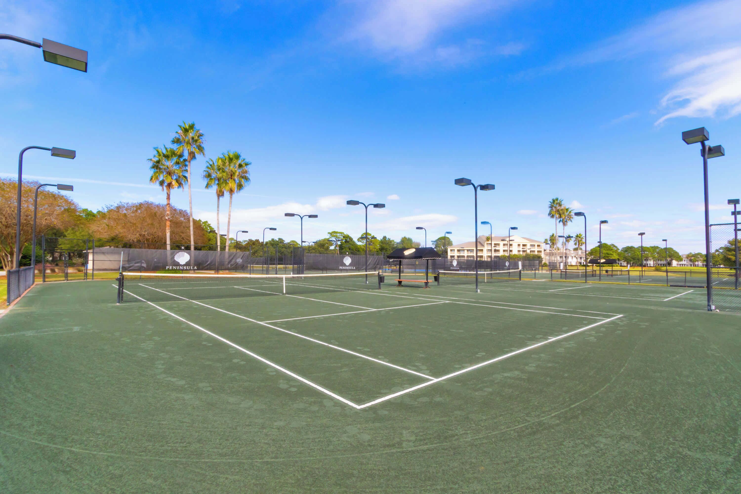 A tennis court with multiple courts, palm trees, and street lamps.