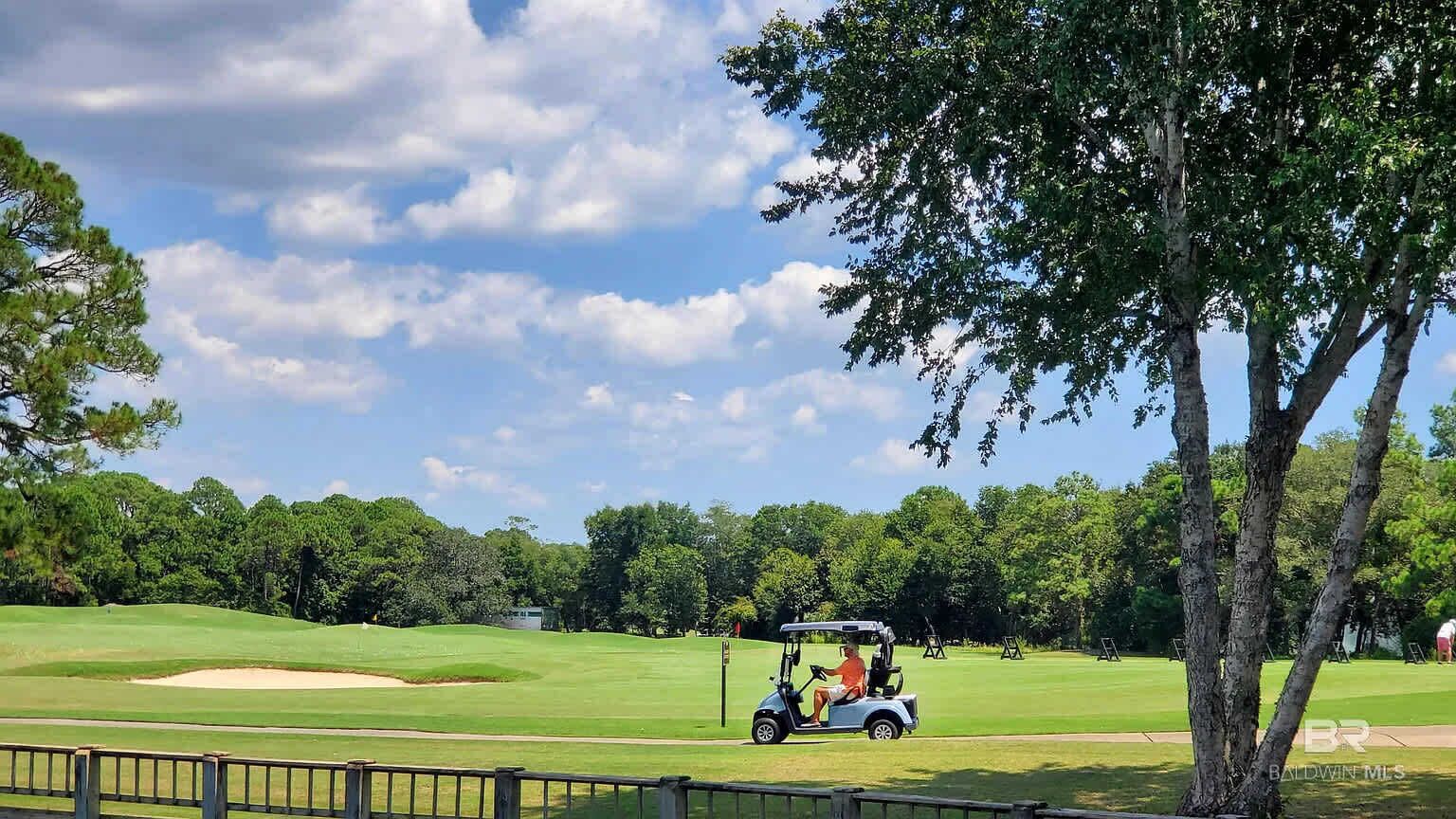 Un campo de golf con un carrito, árboles y cielo despejado.