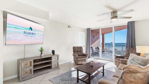 A spacious living room with a large TV, comfortable seating, and a view of the ocean through the sliding glass doors. - Gulf View 2 Bed Beaches Pool Dining and Fun (Gulf Shores)
