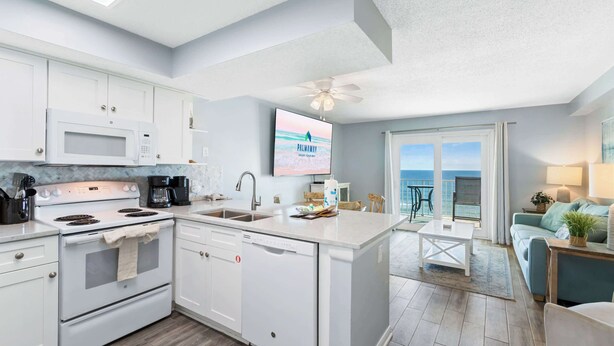 A modern kitchen with white appliances, a large island, and a view of the ocean through the sliding glass doors. - NEW Gulf Front - Beaches Pool Dining and Fun (Gulf Shores)