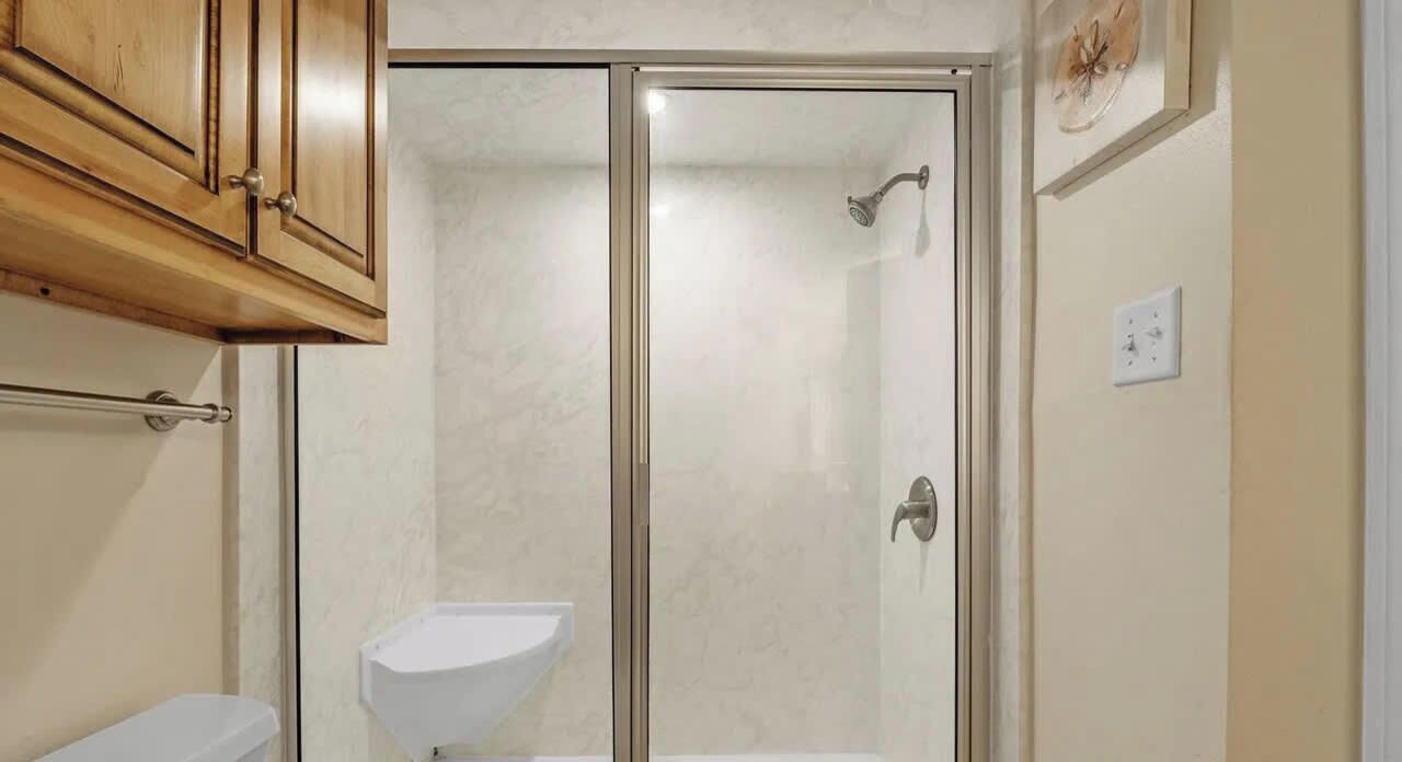 Une salle de bain avec une douche à parois de verre, un lavabo blanc et des meubles en bois.