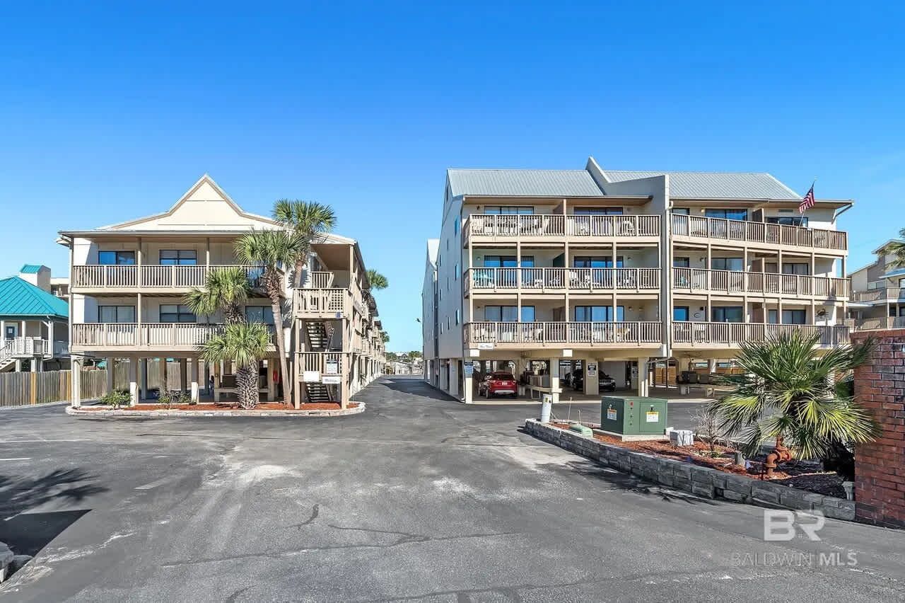 A beachfront hotel with multiple balconies, a parking area, and a clear sky.