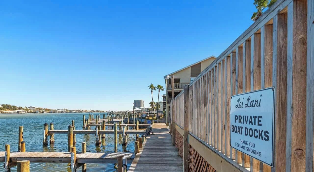 A wooden pier leading to private boat docks with a clear view of the water and distant buildings.