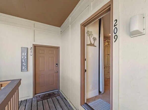 Una terraza de madera que conduce a la entrada de una casa, con una puerta que indica “HOUSE” y el número 209.