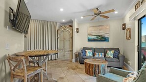 A living room with a grey sofa, a round coffee table, and a TV mounted on the wall. - 1 bed Beach Pools Waterfront Boating Palmaway (Orange Beach)