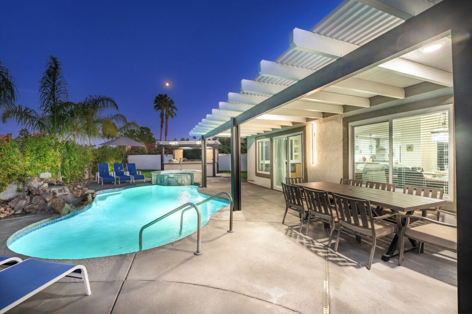 Un espace piscine comprenant un jacuzzi, des chaises longues et un coin repas couvert avec une table et des chaises.