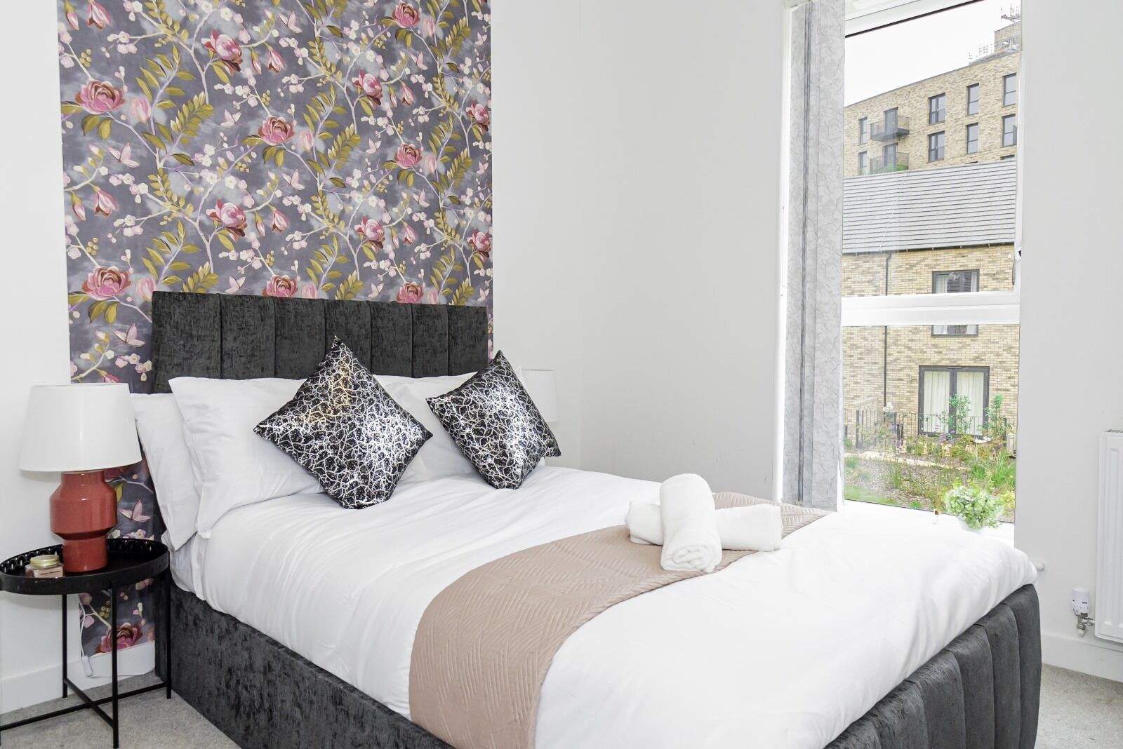 A neatly made bed with white linens, two patterned pillows, and a beige throw blanket.