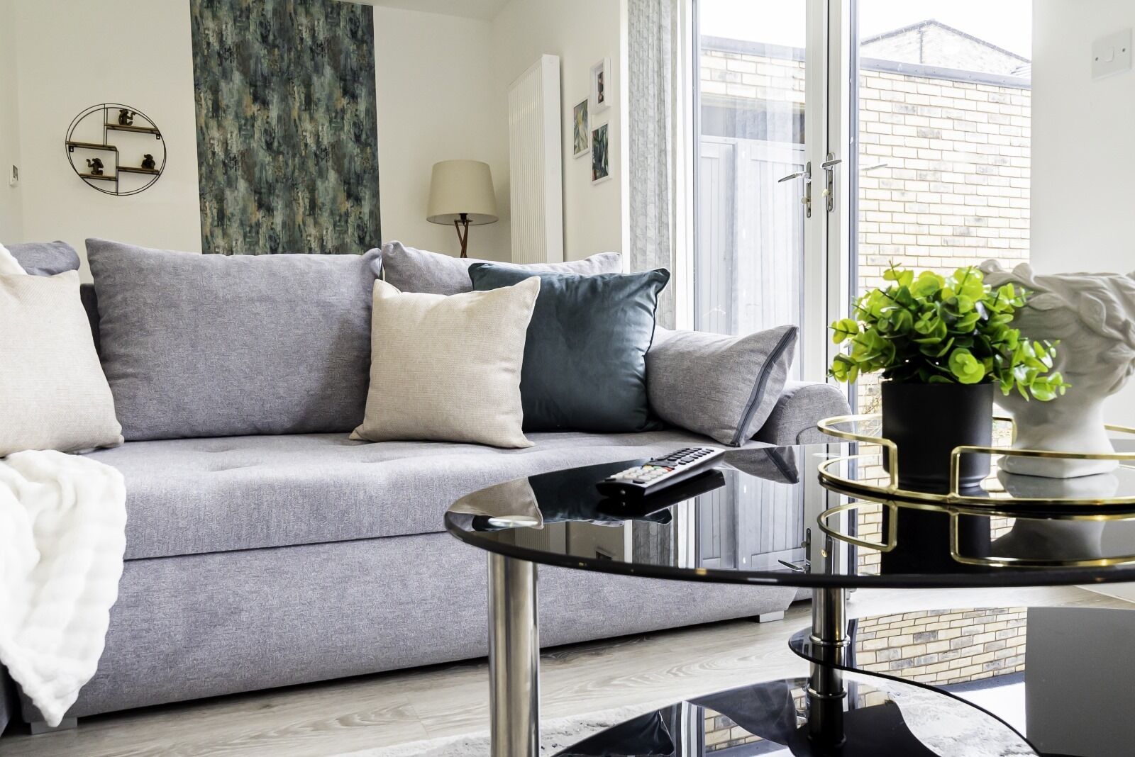 A modern living room with a grey sofa, a glass coffee table, and a potted plant.