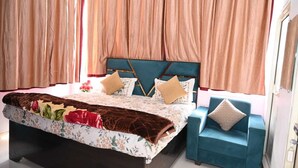 A bedroom with a bed, two pillows, a bedside table, and a chair. - Shri Dham Hotel And Resort (Ayodhya)