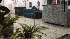 A reception area with a reception desk, a seating area with a sofa, and a large window. - Shri Dham Hotel And Resort (Ayodhya)