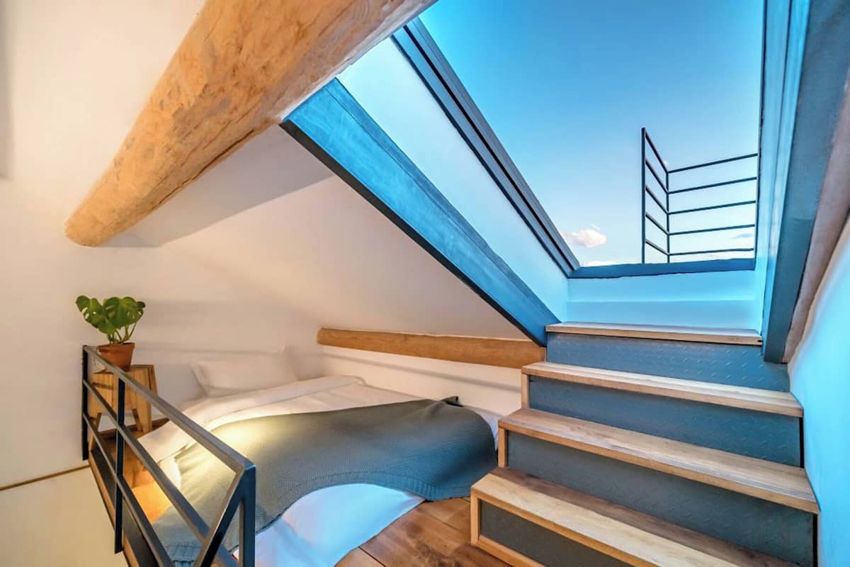 Un dormitorio con tragaluz, escalera de madera y una cama.