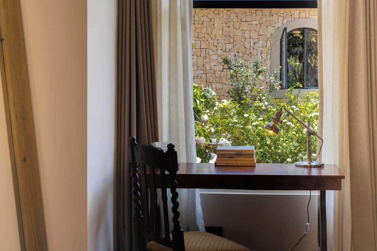 Una habitación con escritorio de madera, una silla, una lámpara y una ventana con cortinas.