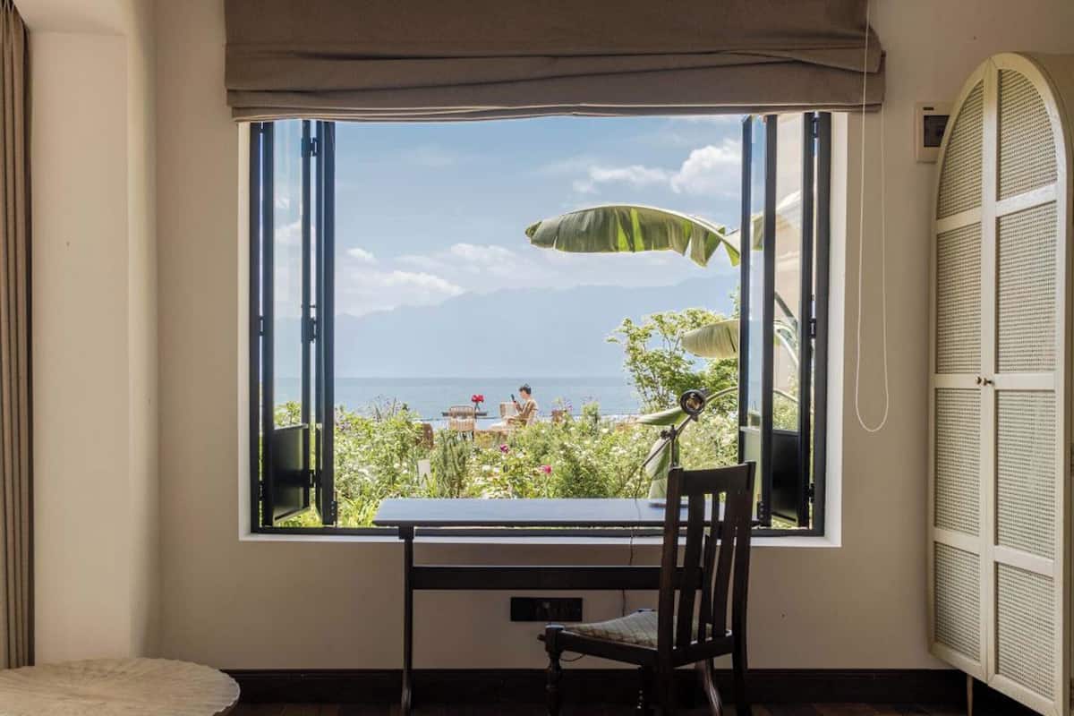 Una habitación con un ventanal grande que da a un jardín y al mar.
