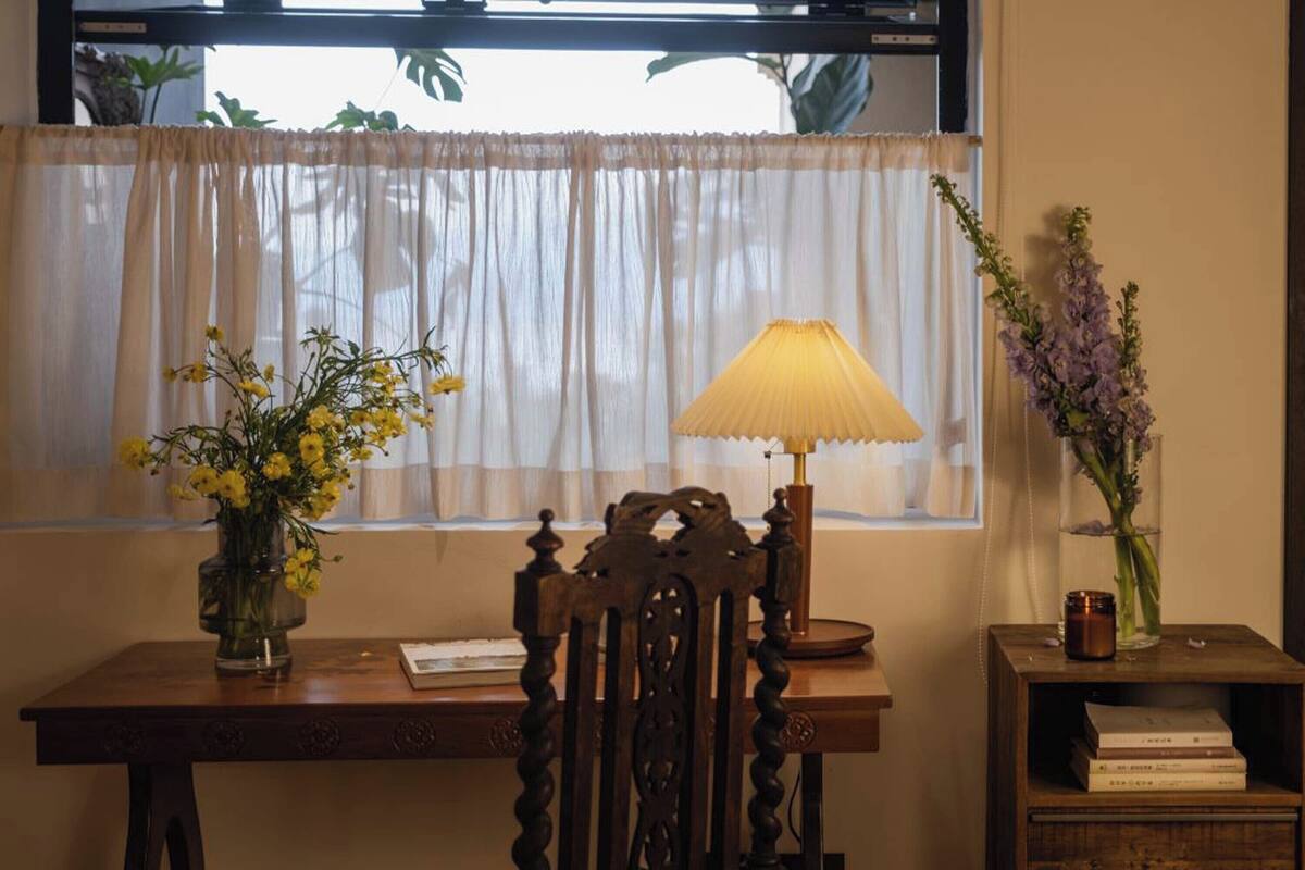 Un escritorio de madera con una lámpara, un jarrón con flores amarillas y un jarrón con flores moradas.