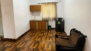 A room with a herringbone wooden floor, a sofa, a cabinet, a television, and a window with curtains. - Celeste Stays (Candolim)