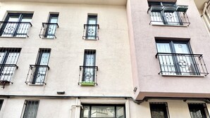 A multi-story building with a central entrance featuring ornate metal gates, multiple balconies with black railings, and a tiled pavement in front. - New apartment in the heart of Istanbul – near Istiklal and Galata (İstanbul)